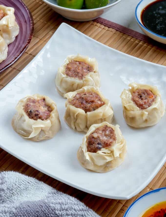 pork siomai on a white plate with calamansi and soy sauce on the side