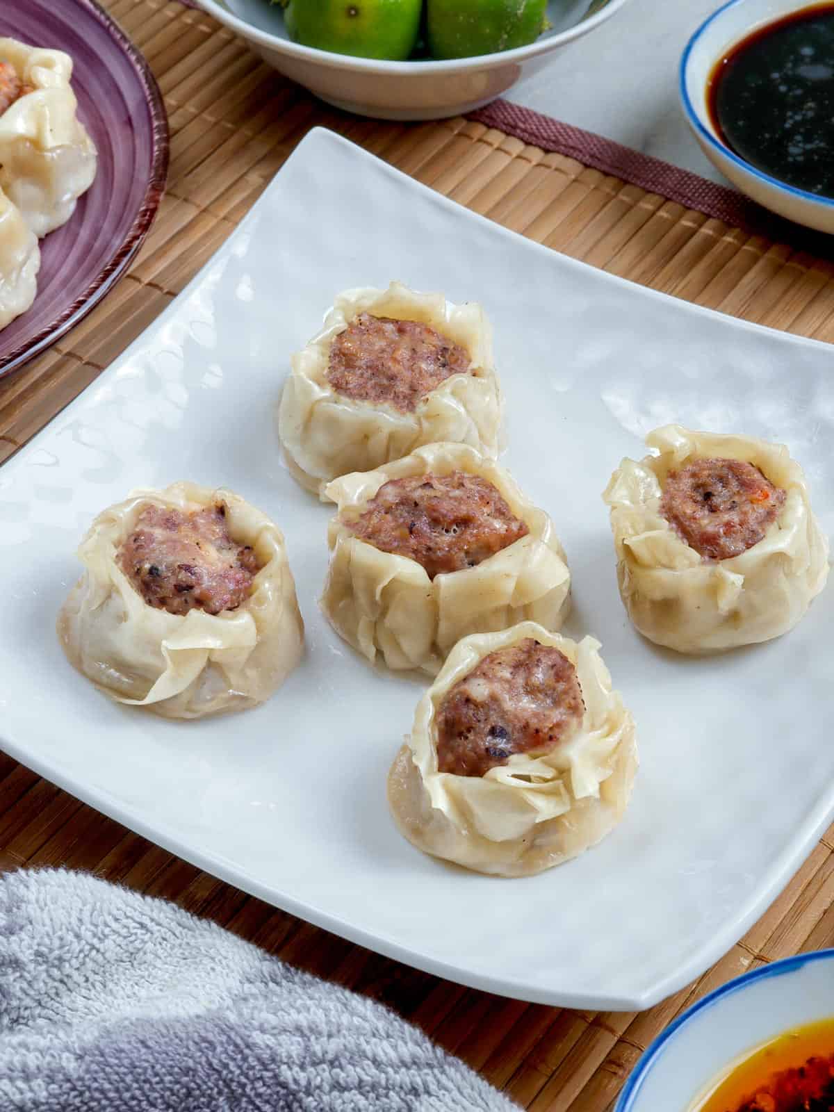 pork siomai on a white plate with calamansi and soy sauce on the side