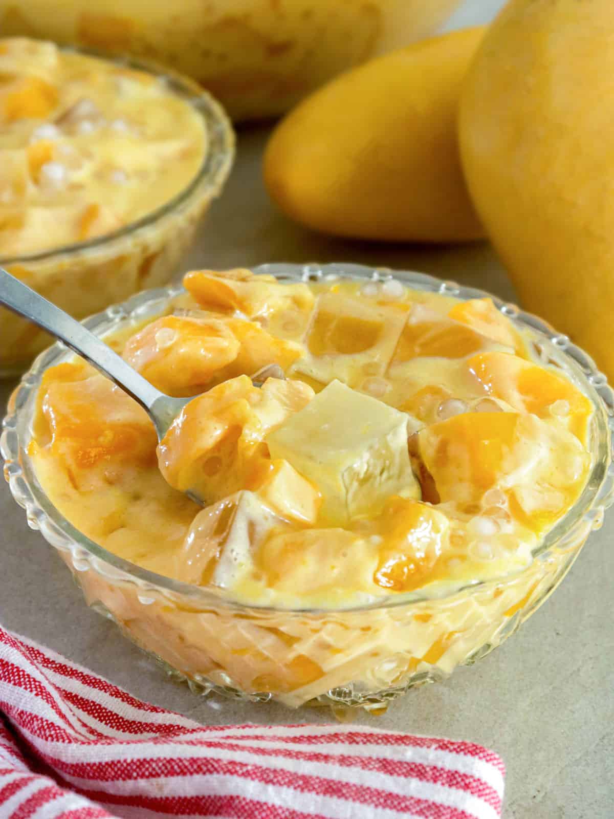 eating mango jelly in a bowl with fresh mangoes in the background.