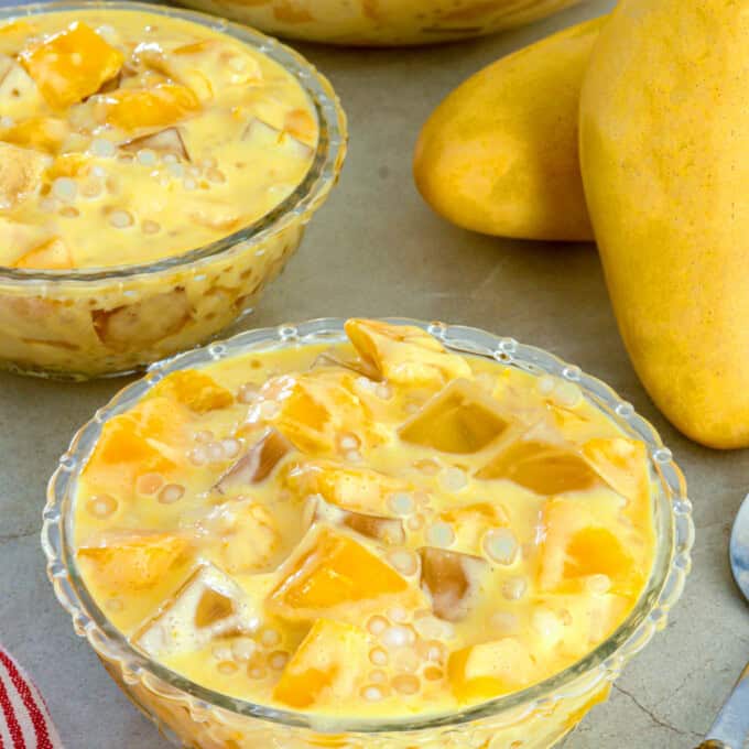 mango sago jelly in clear glass bowls with fresh mangoes in the background.