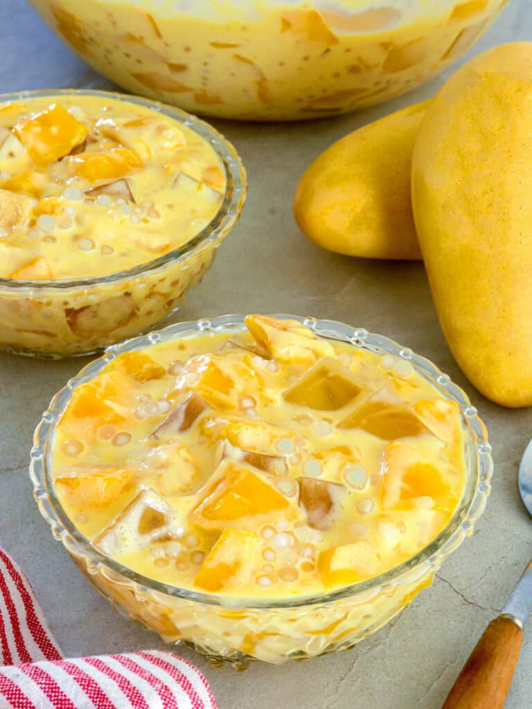 mango sago jelly in clear glass bowls with fresh mangoes in the background.