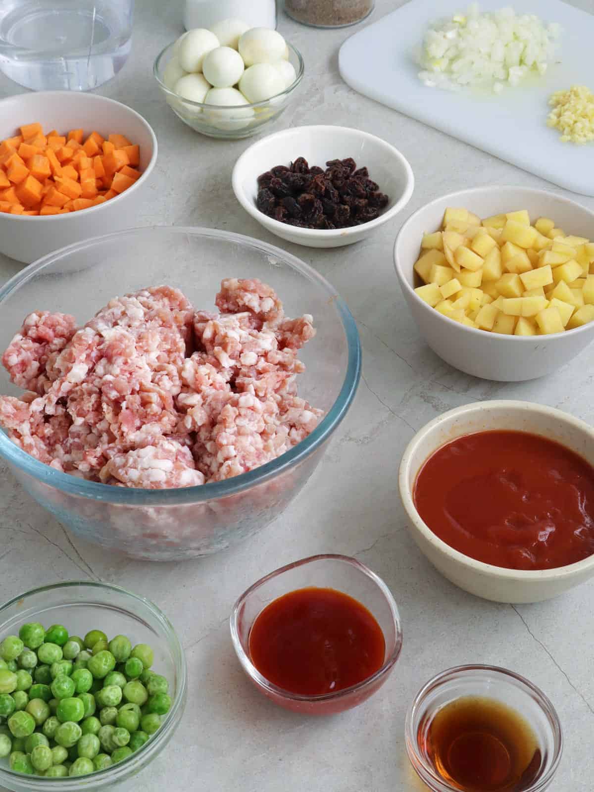 ground pork, diced carrots, diced potatoes, green peas, raisings, tomato sauce, banana ketchup, quail eggs in individual bowls