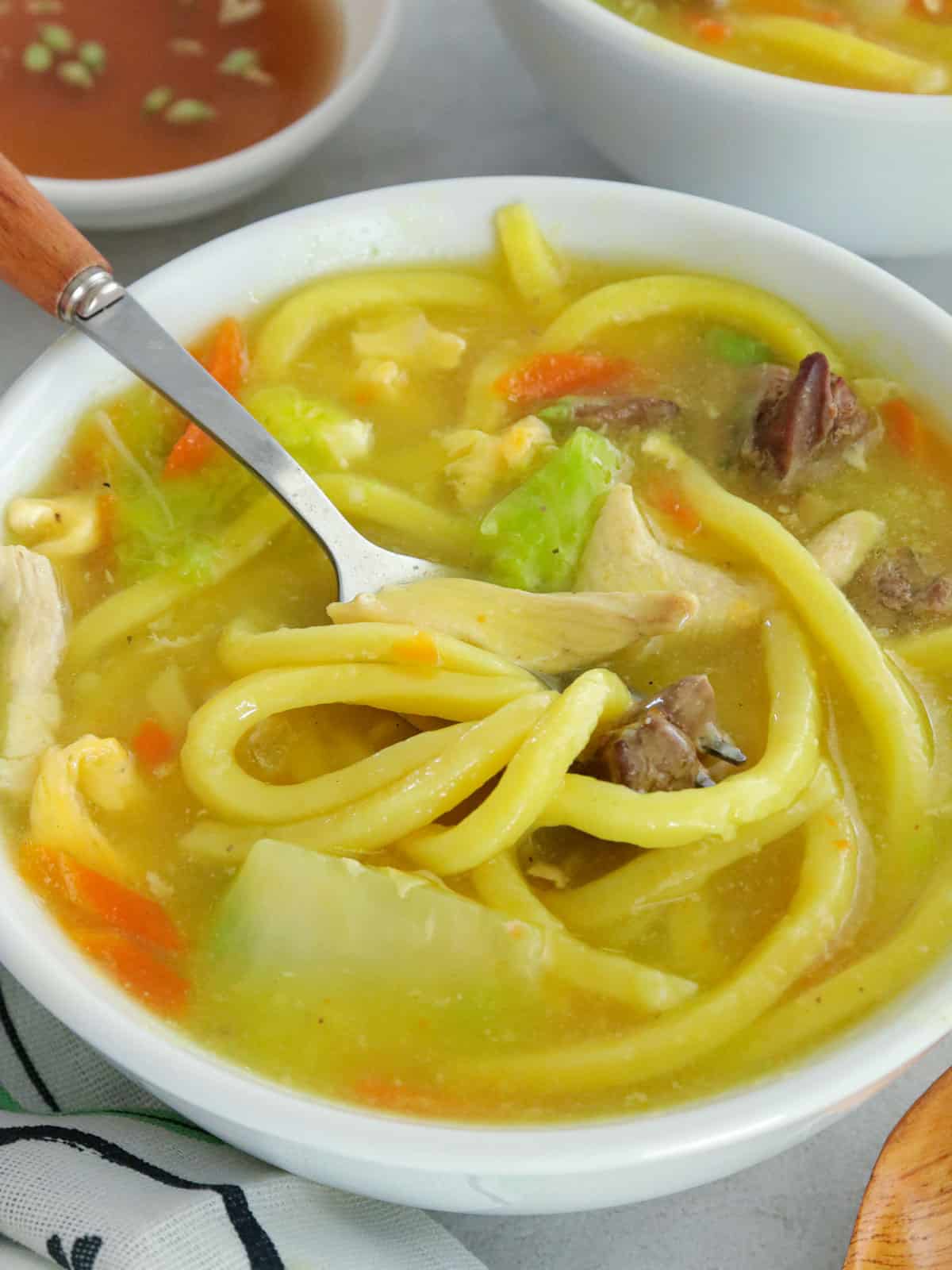 eating lomi soup from a white bowl.