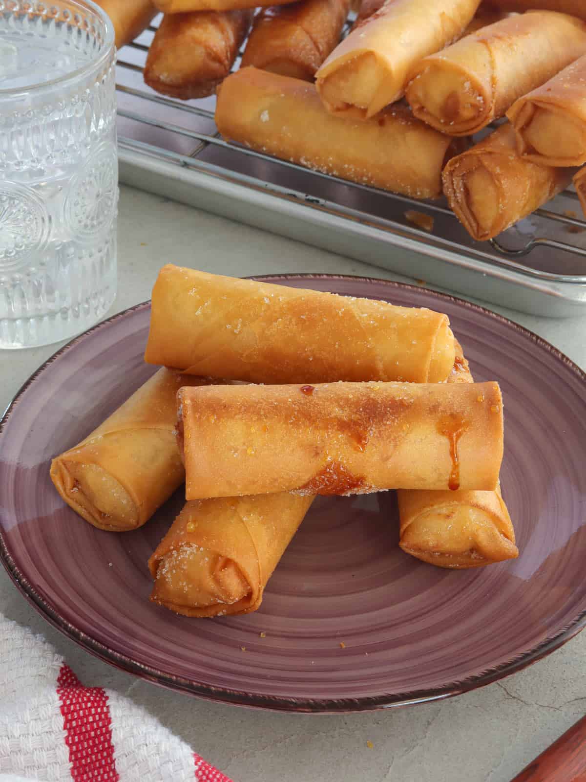 Turon Malagkit on a serving plate with glass of water in the background.