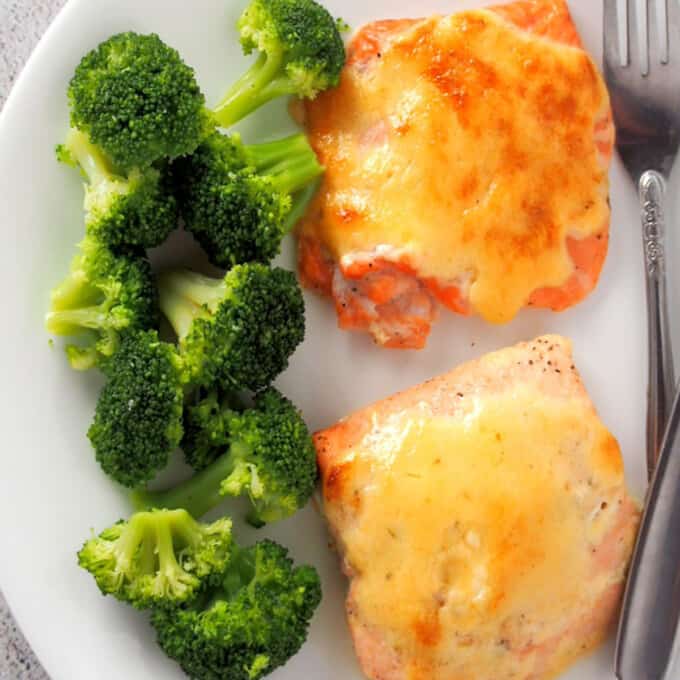 top view of baked salmon with tamarind mayo topping on white plate with steamed broccoli florets