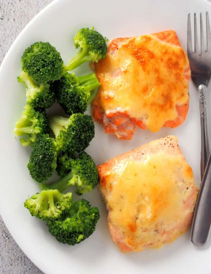 top view of baked salmon with tamarind mayo topping on white plate with steamed broccoli florets