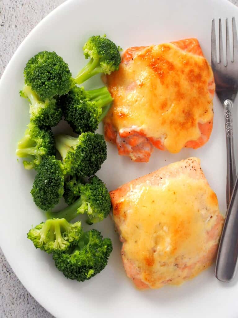 top view of baked salmon with tamarind mayo topping on white plate with steamed broccoli florets