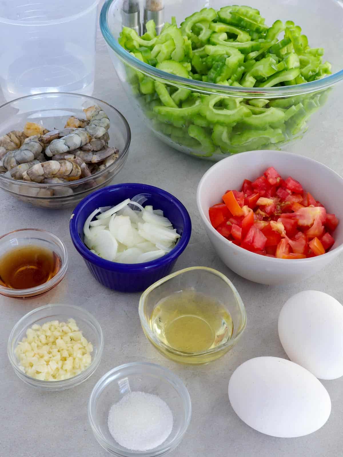 sliced bittermelon, shrimp, tomatoes, eggs, salt, pepper, fish sauce, onions, garlic in bowls