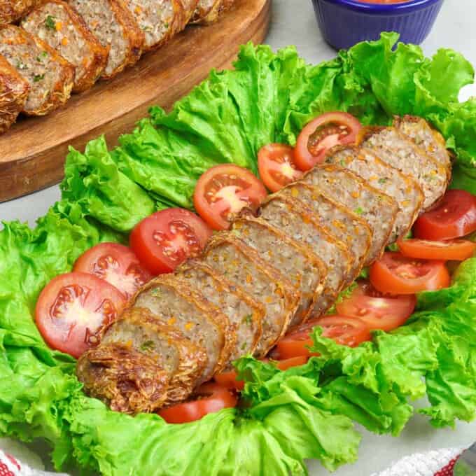 sliced Homemade Kikiam on a serving platter garnished with lettuce leaf and sliced tomatoes