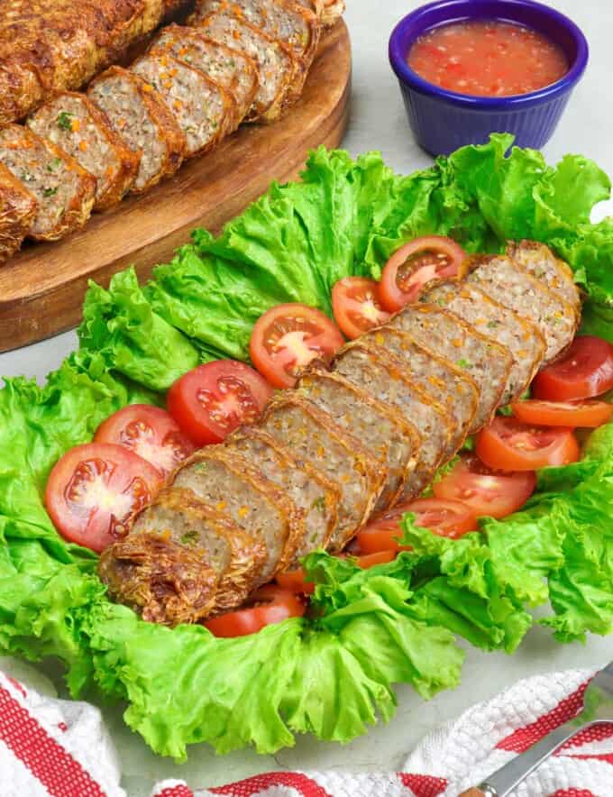 sliced Homemade Kikiam on a serving platter garnished with lettuce leaf and sliced tomatoes