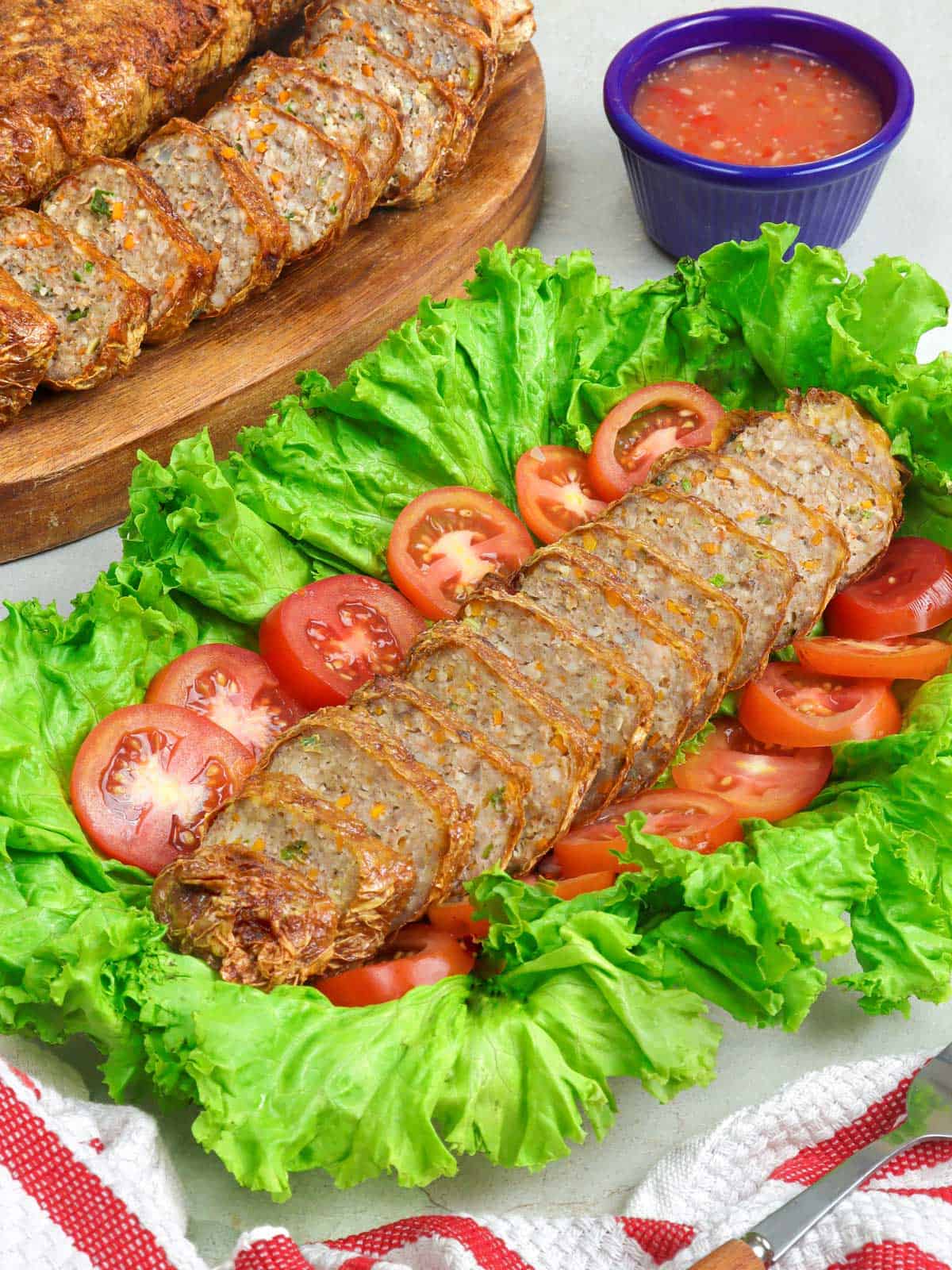 sliced Homemade Kikiam on a serving platter garnished with lettuce leaf and sliced tomatoes