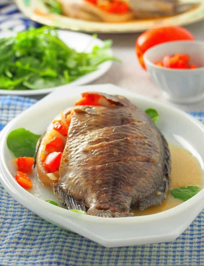 Pinaputok na Tilapia on a serving platter with a plate of green salad on the side