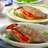 Filipino-style oven-baked tilapia stuffed with tomatoes and onions on a white serving platter