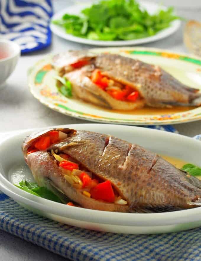 Filipino-style oven-baked tilapia stuffed with tomatoes and onions on a white serving platter