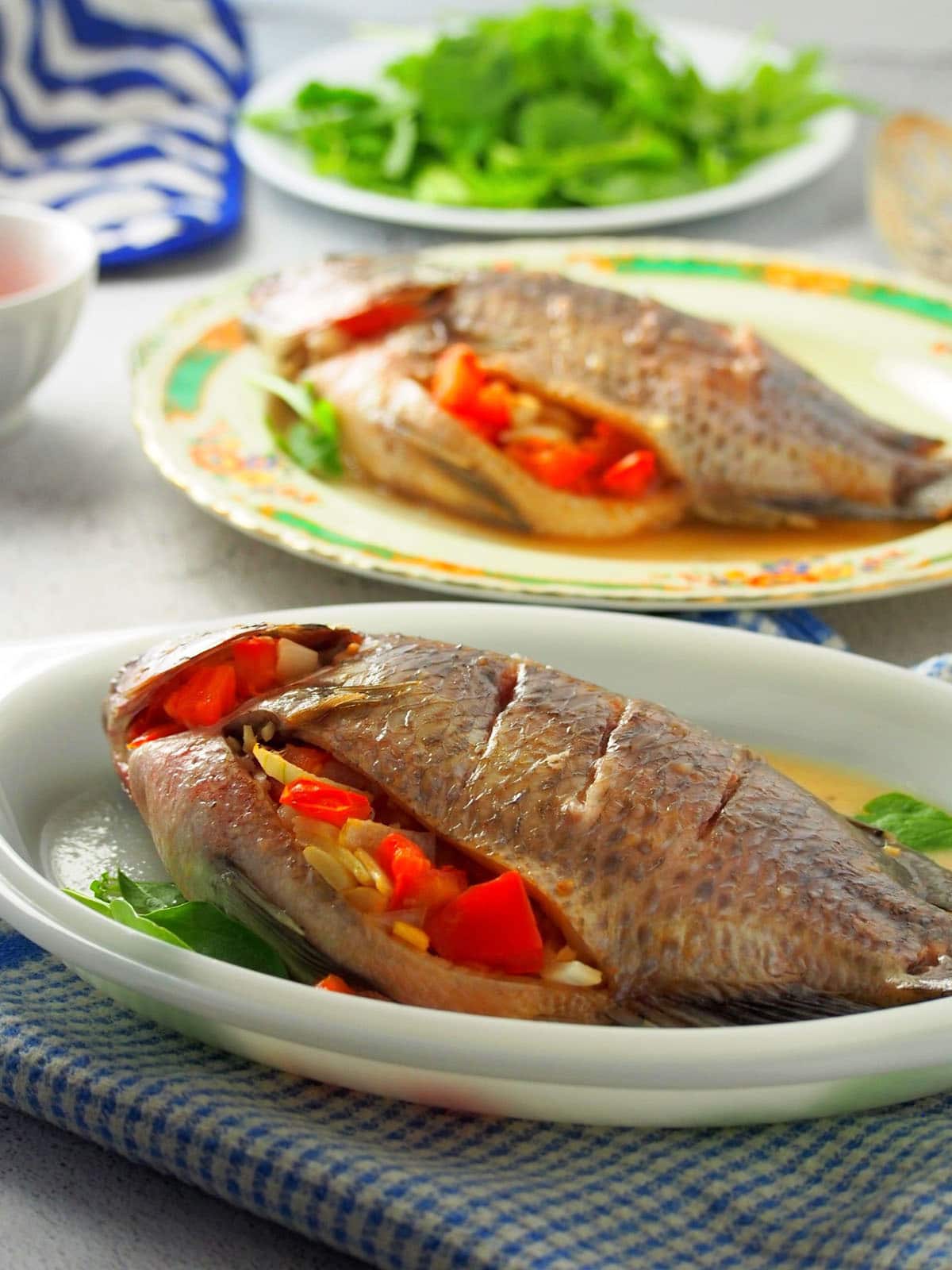 Filipino-style oven-baked tilapia stuffed with tomatoes and onions on a white serving platter