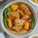 pocherong baboy with pork and beans, banana, potatoes, carrots and pechay in a white bowl with a plate of steamed rice on the side