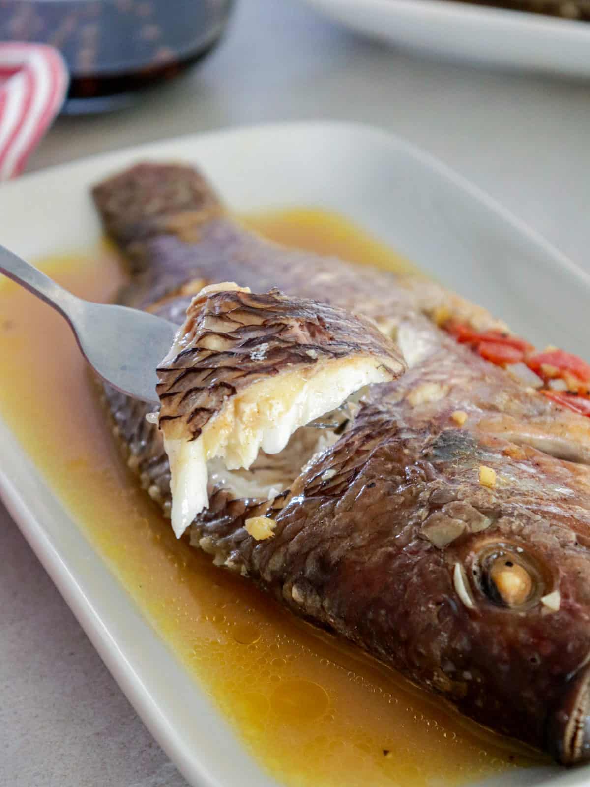 eating baked stuffed tilapia with a fork from a white platter.