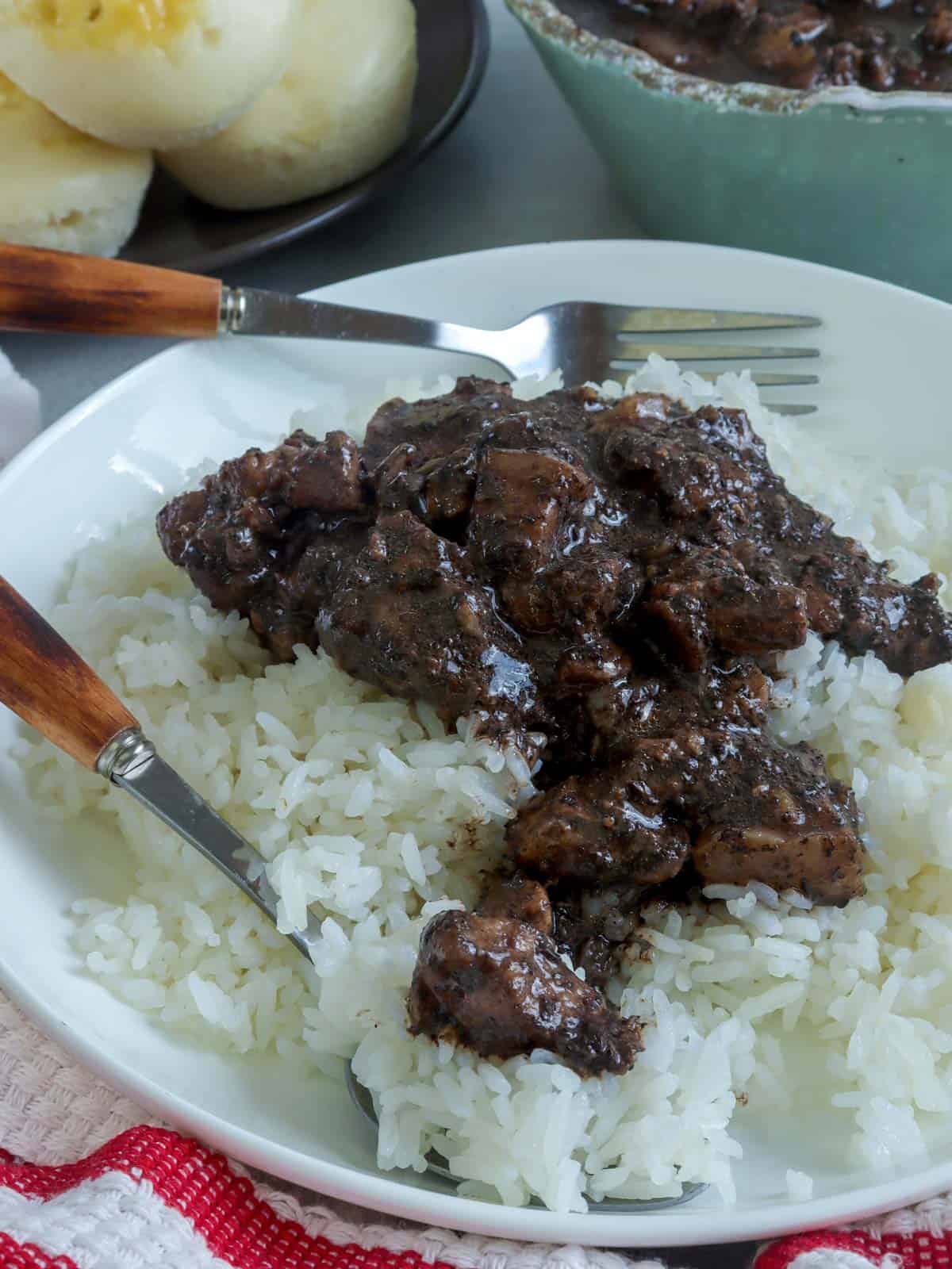 dinuguan over steamed rice on a white serving plate