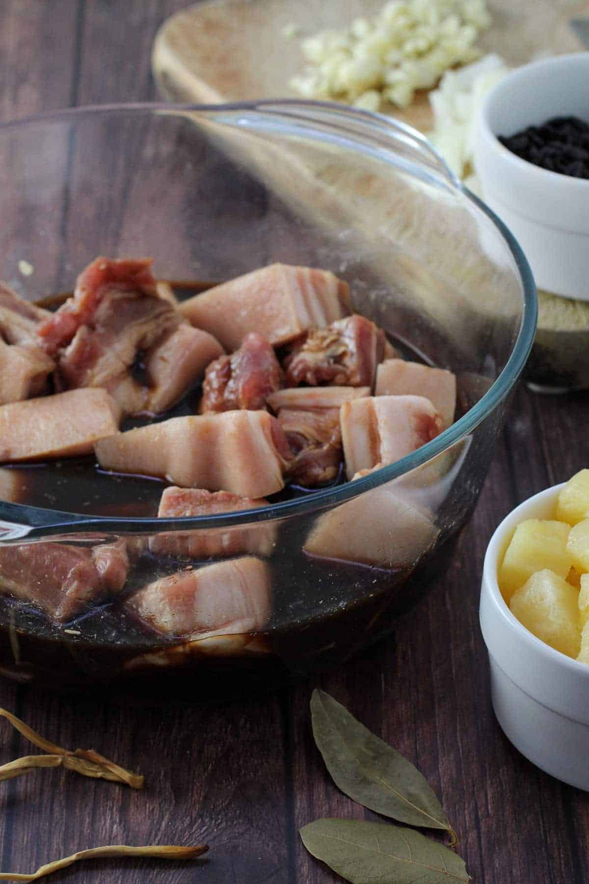 marinating pork belly in soy sauce mixture in a clear glass bowl