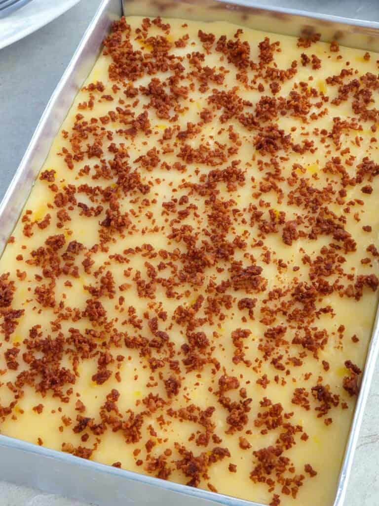 maja langka with latik topping in an aluminum baking pan with a plate of sliced piece of maja on the side