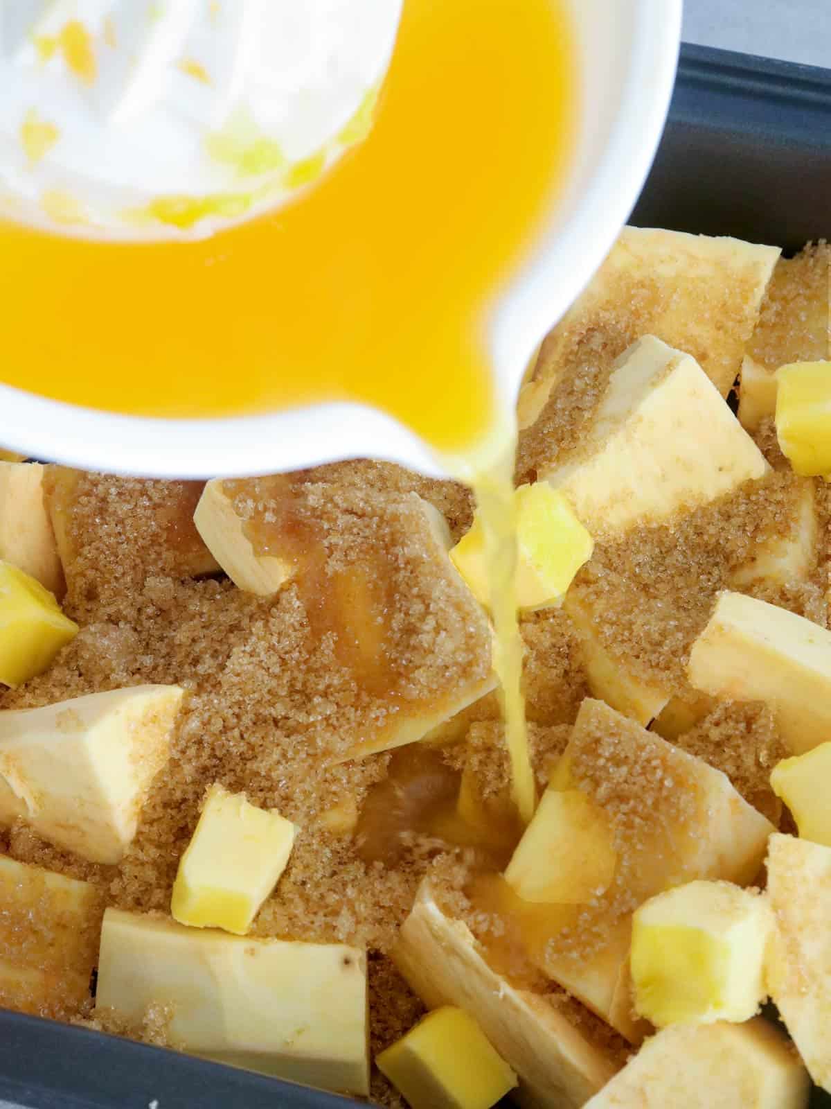 pouring orange juice on cut sweet potatoes with butter and brown sugar in a baking dish