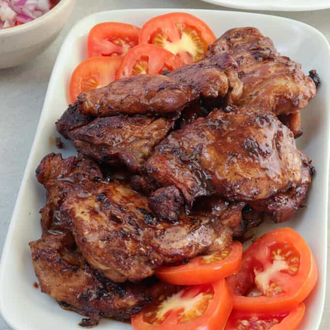 cooked chicken tapa on a white serving platter with sliced tomatoes.