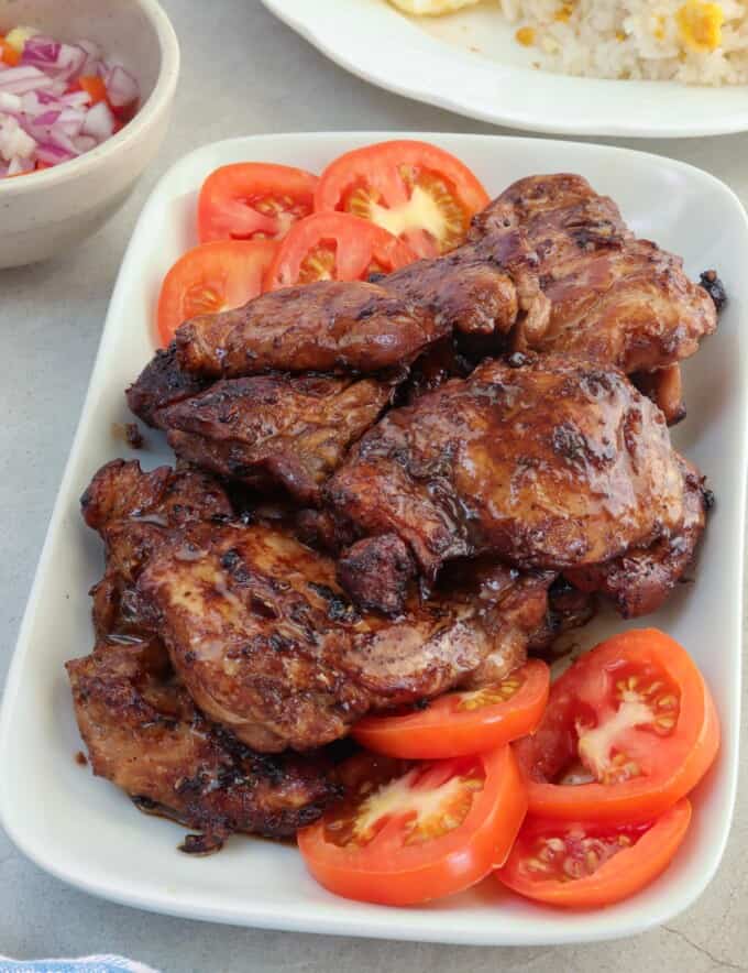 cooked chicken tapa on a white serving platter with sliced tomatoes.