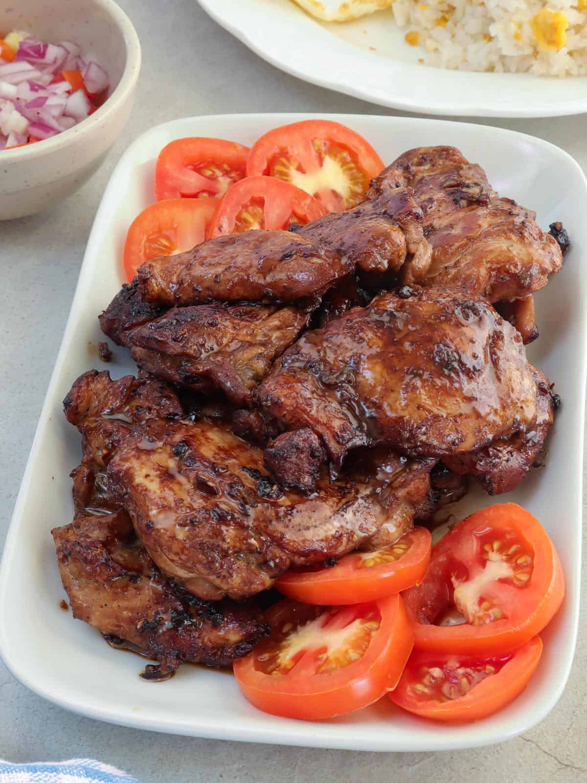 cooked chicken tapa on a white serving platter with sliced tomatoes.