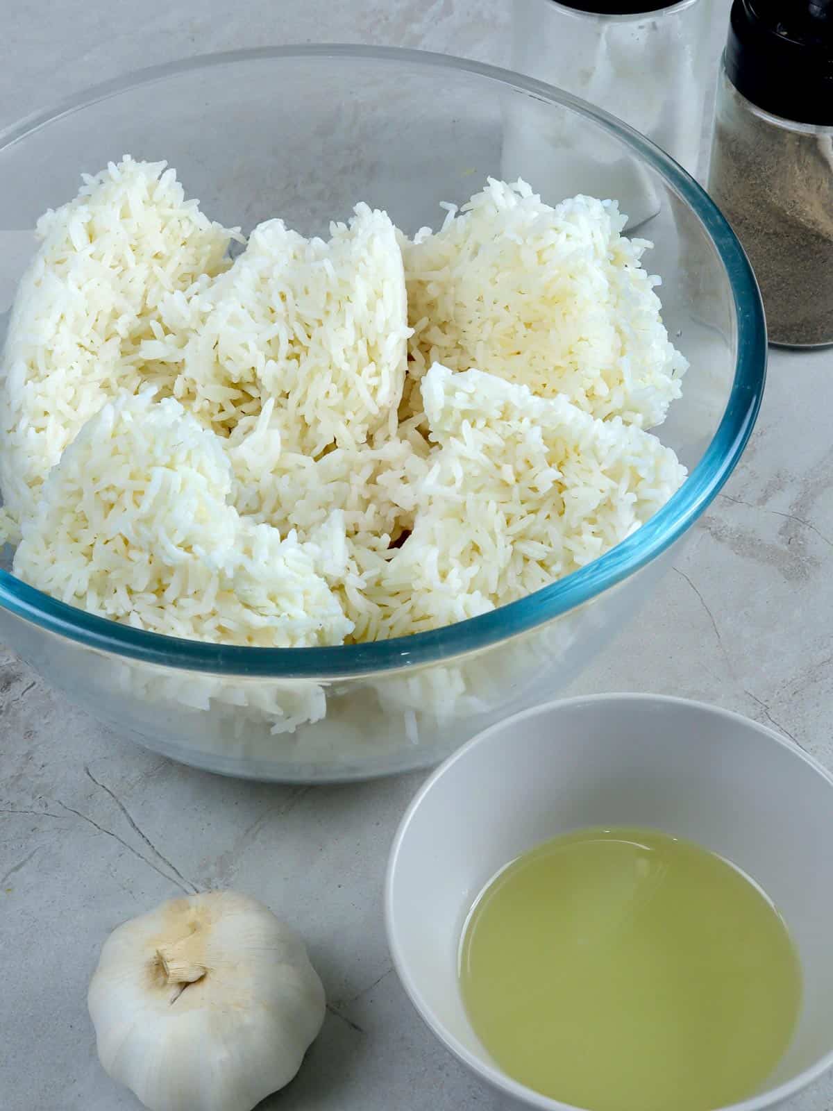 steamed rice in a bowl, garlic head, oil, salt, and pepper