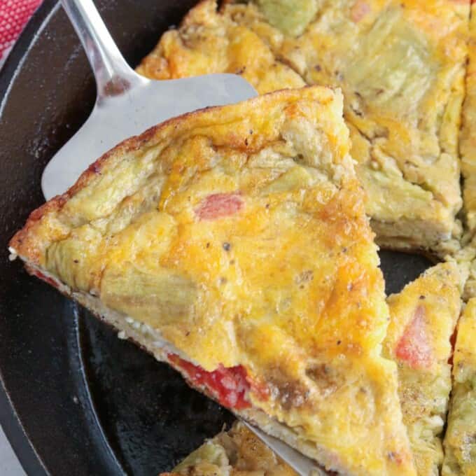 serving a slice of eggplant and tomato frittata from a cast iron skillet.