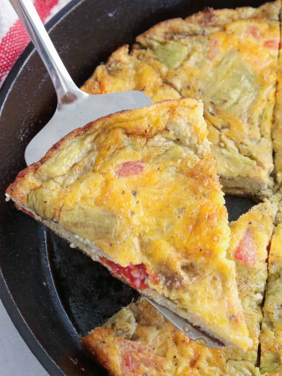 serving a slice of eggplant and tomato frittata from a cast iron skillet.