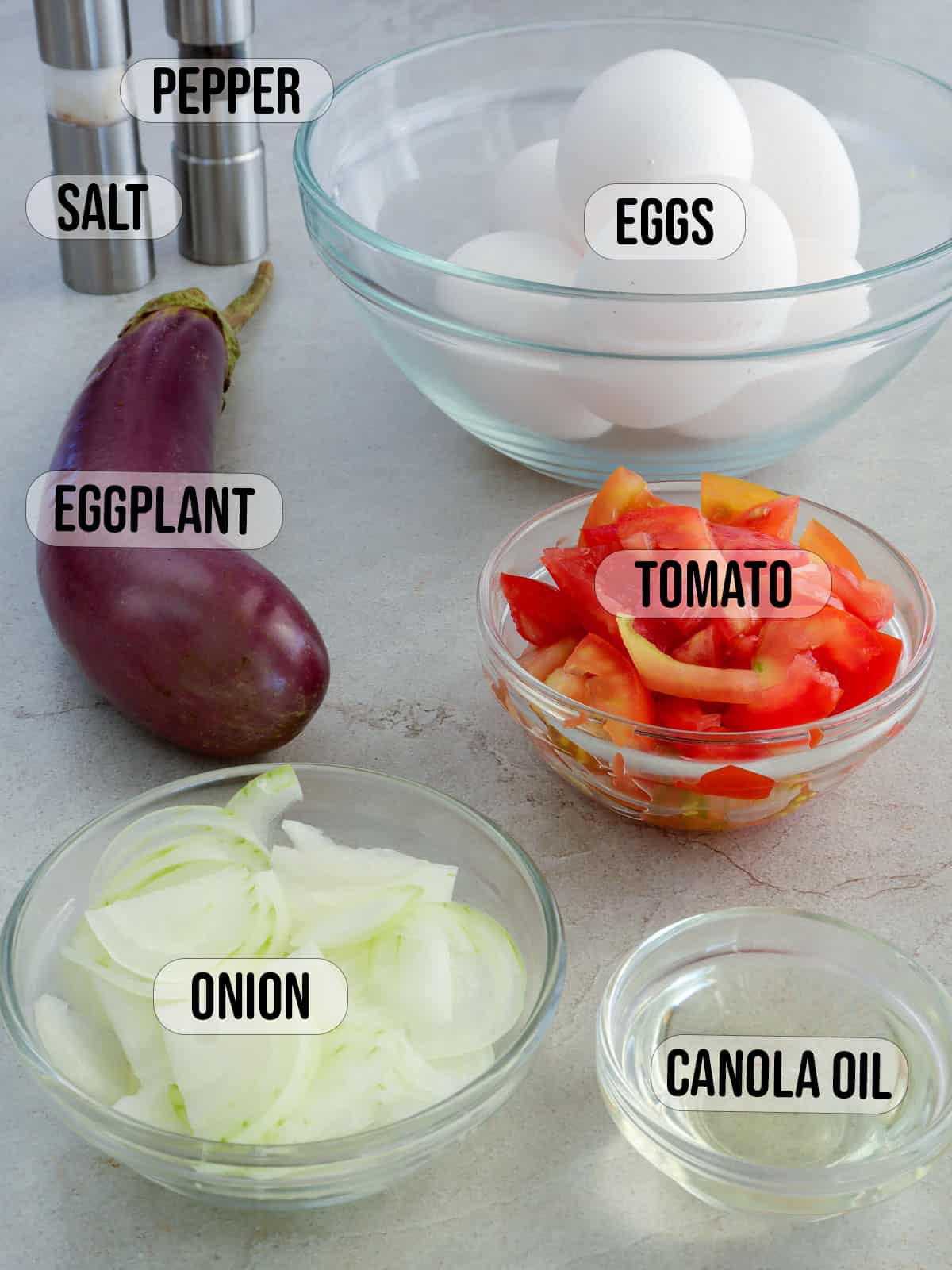 eggplant, chopped tomatoes, onions, oil, and eggs in bowls with salt and pepper shakers in the background.