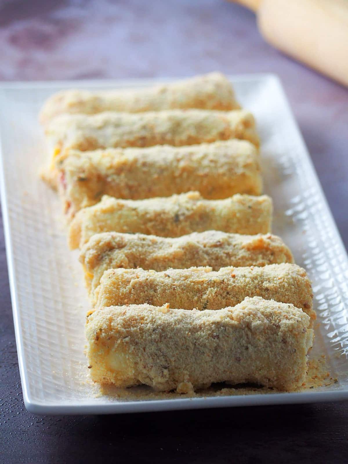 rolling ham and cheese bread rolls on a white platter ready to fry