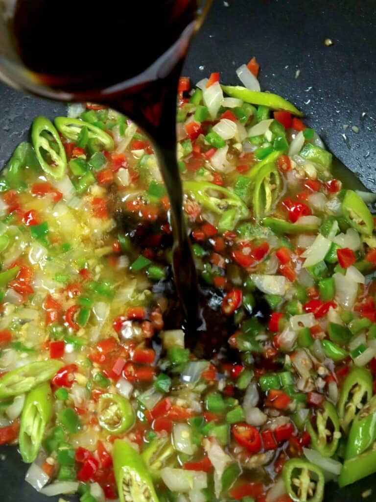 pouring knorr seasoning on sauteed peppers and onions in a pan