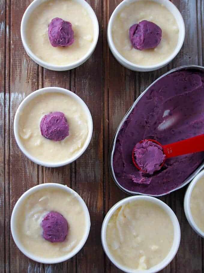 placing ube halaya on top of cassava cake mixture to make ube cassava cake in white ramekins