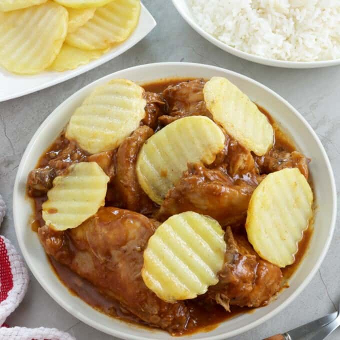 chicken asado with pan-fried potatoes in a white serving bowl with a plate of steamed rice on the side