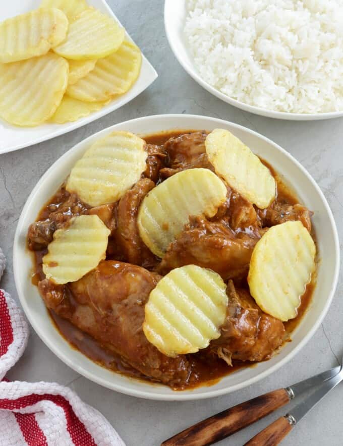 chicken asado with pan-fried potatoes in a white serving bowl with a plate of steamed rice on the side