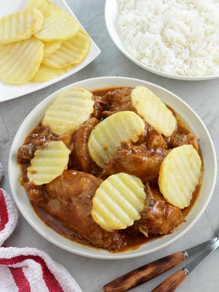 chicken asado with pan-fried potatoes in a white serving bowl with a plate of steamed rice on the side