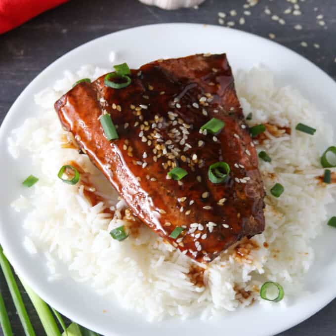 top-view shot of pan-fried salmon with teriyaki glaze over a bed of steamed rice on a black serving plate