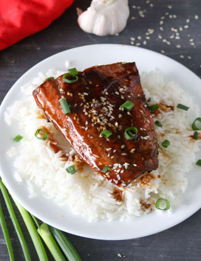 top-view shot of pan-fried salmon with teriyaki glaze over a bed of steamed rice on a black serving plate