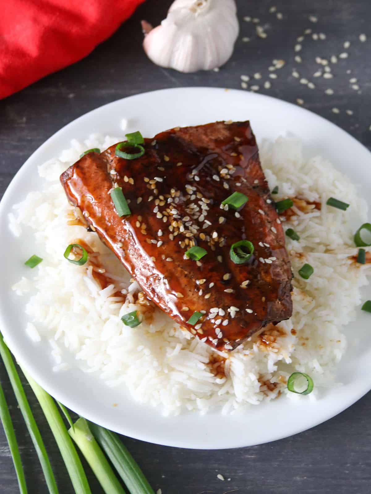top-view shot of pan-fried salmon with teriyaki glaze over a bed of steamed rice on a black serving plate