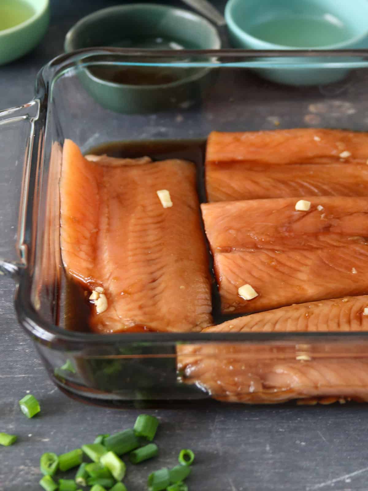 salmon fillets marinating in teriyaki sauce in a light blue bowl