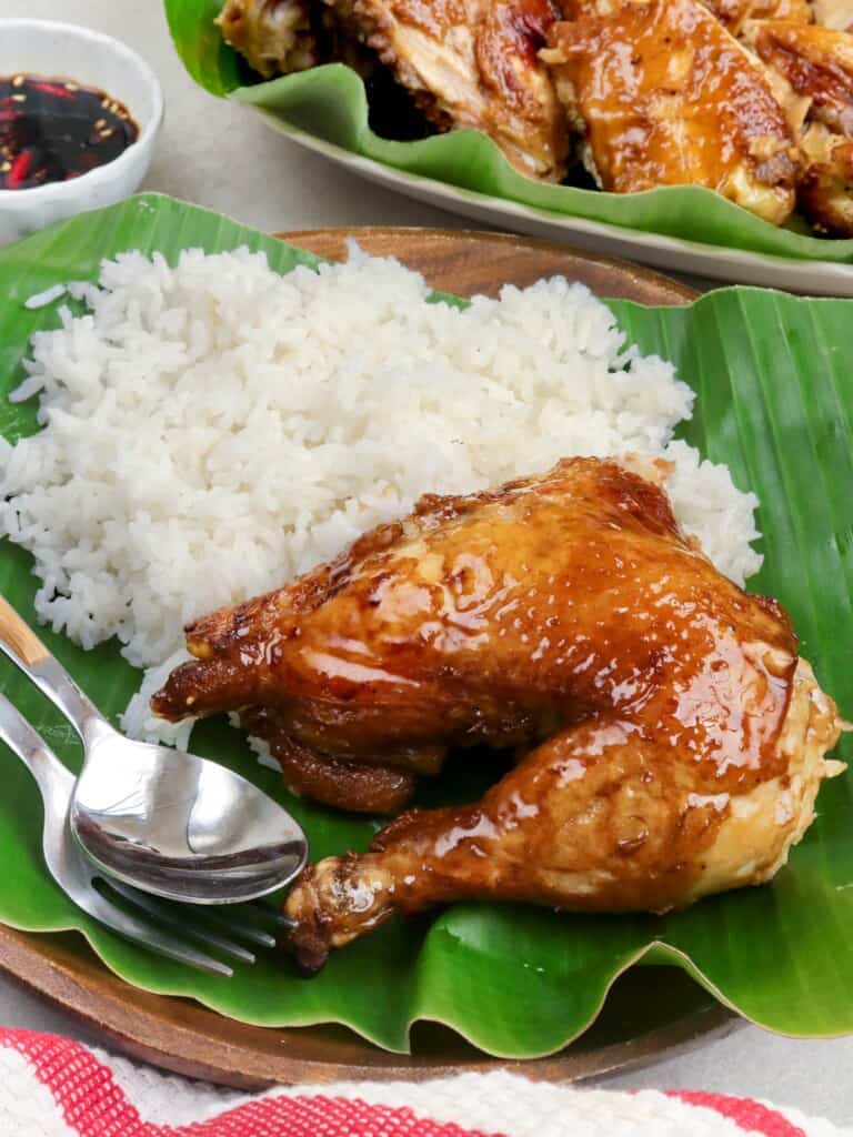 filipino-style roasted chicken leg with steamed rice on a white plate