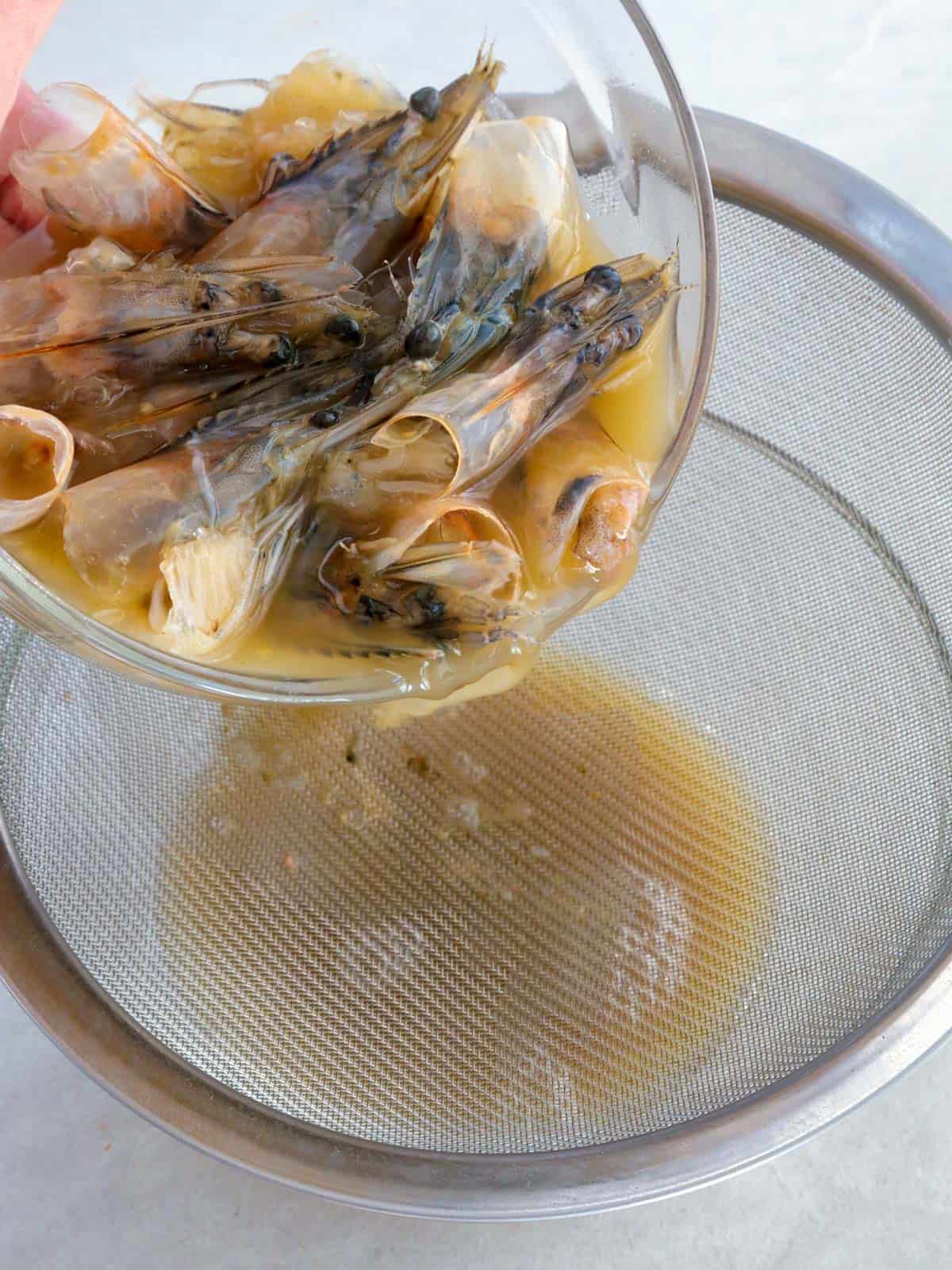 straining juice from shrimp heads ina bowl