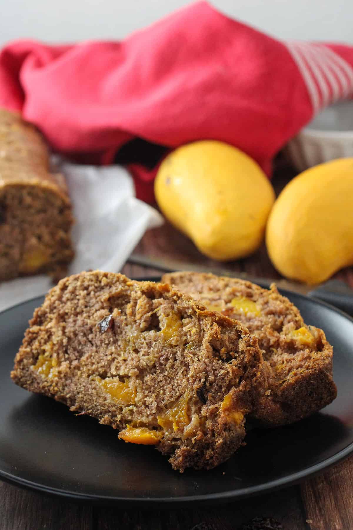 slices of Mango Bread on a black serving plate with fresh mangoes on the side