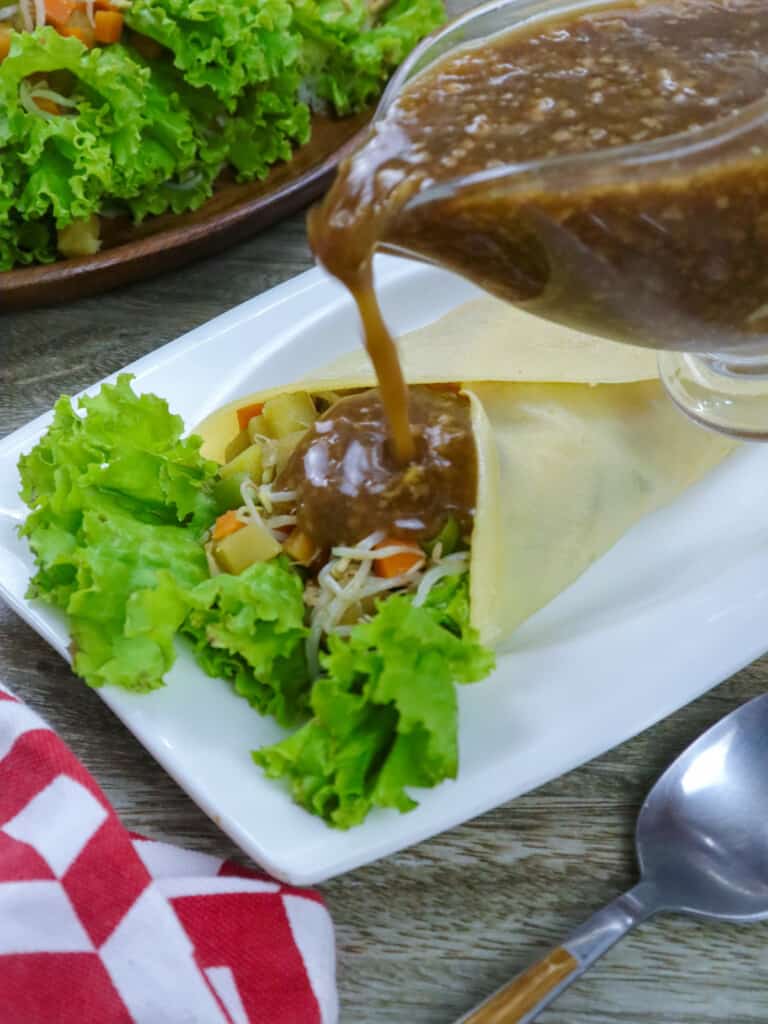 pouring peanut sauce on fresh lumpia on a plate