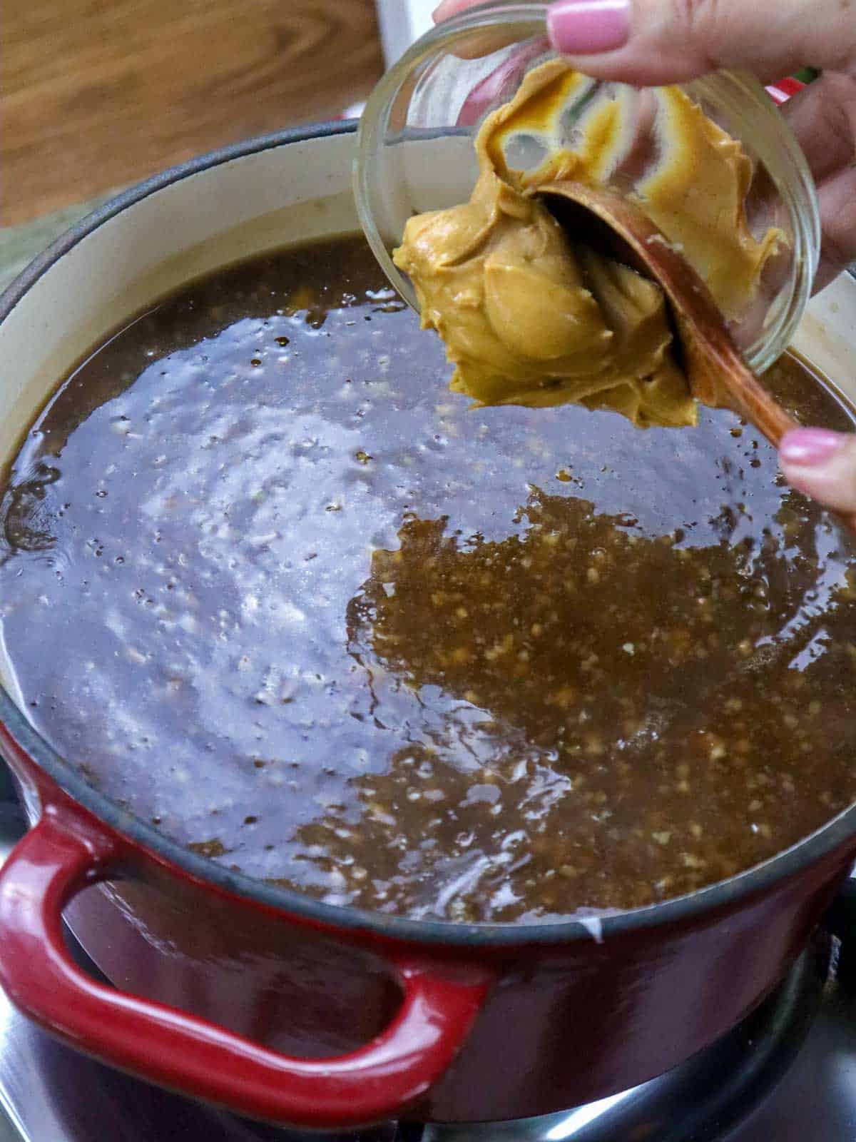 adding peanut butter to a pot of lumpia sauce