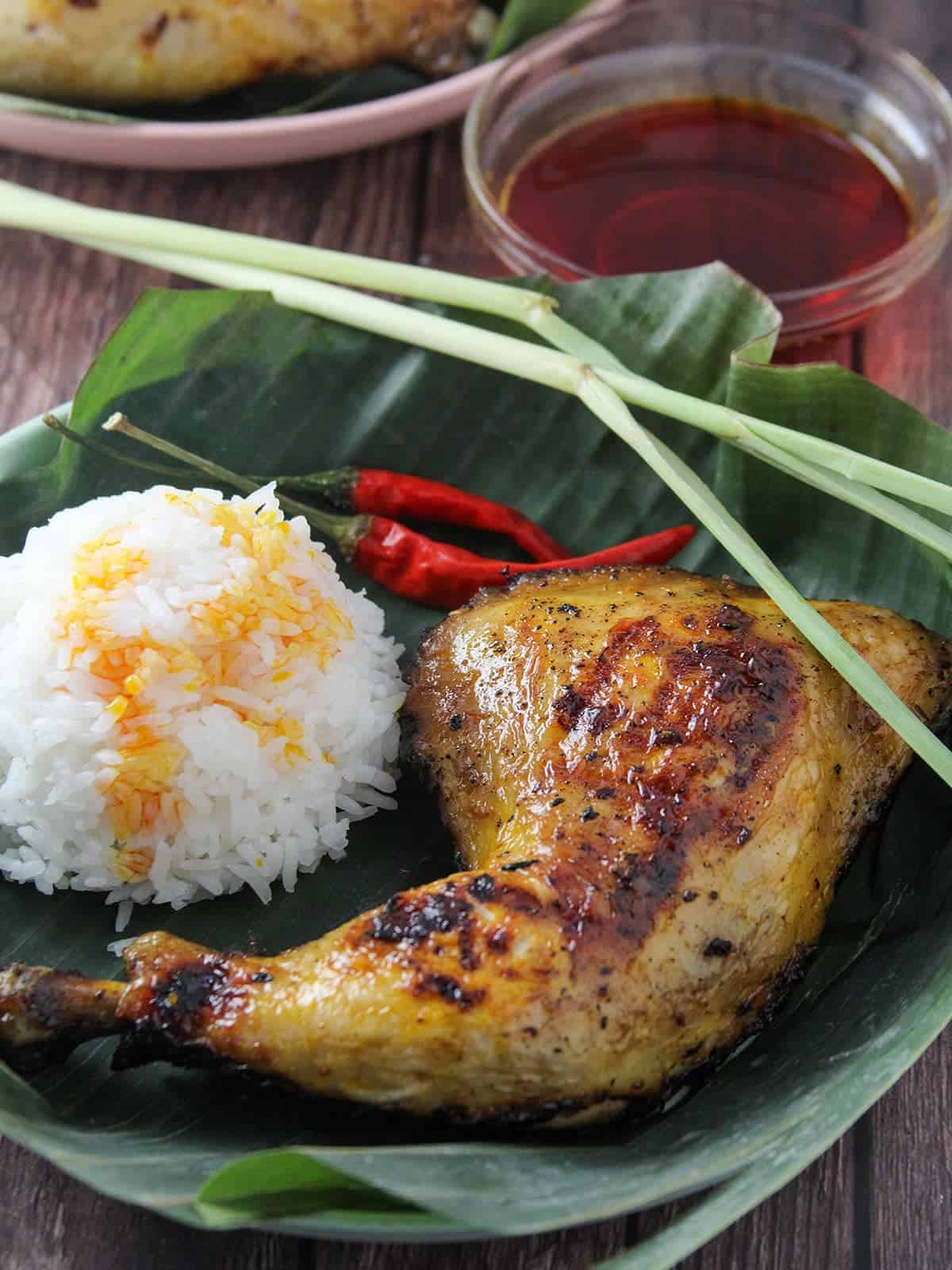 chicken inasal with steamed rice and chicken oil on a banana leaf-lined wooden plate