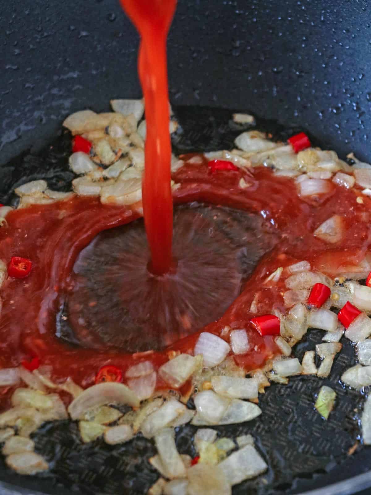 adding tomato sauce to sauteed onions in a pan