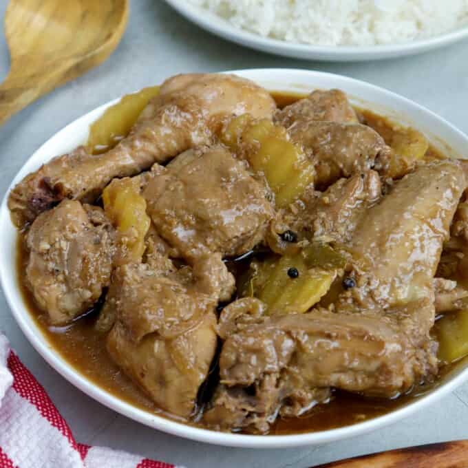 Chicken Adobo with potatoes in a serving bowl with a plate of steamed rice on the side